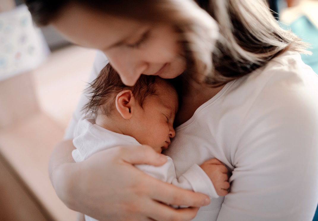 A close-up of a mother holding a newborn baby son at home. A young woman cuddling her new baby boy or girl with love.